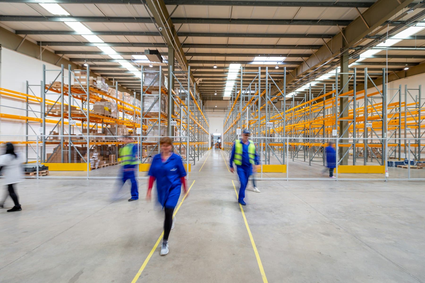 Allée d'entrepôt logistique avec rayonnages et opérateurs en gilet de sécurité