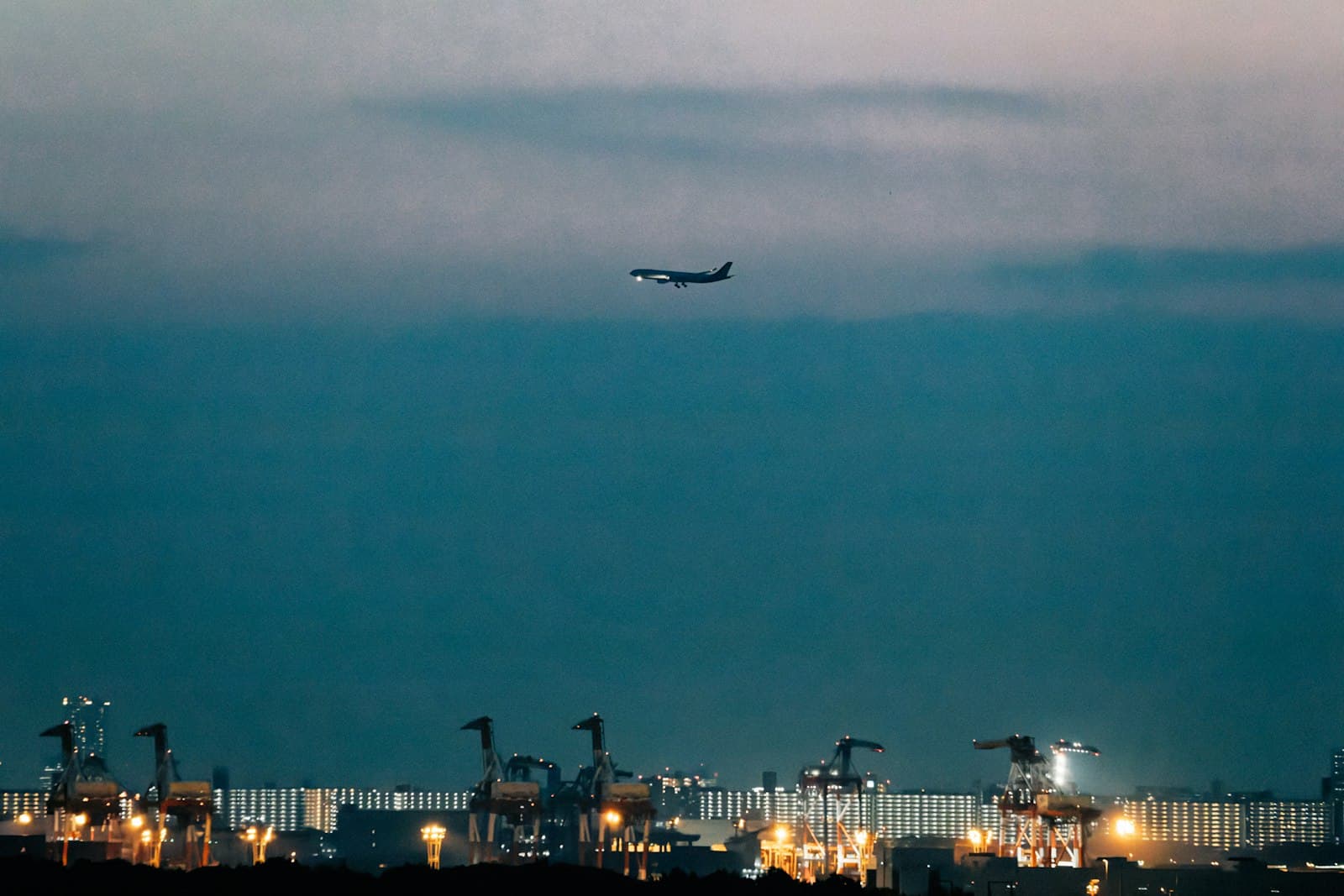 Avion de ligne survolant un terminal portuaire à conteneurs illuminé au crépuscule